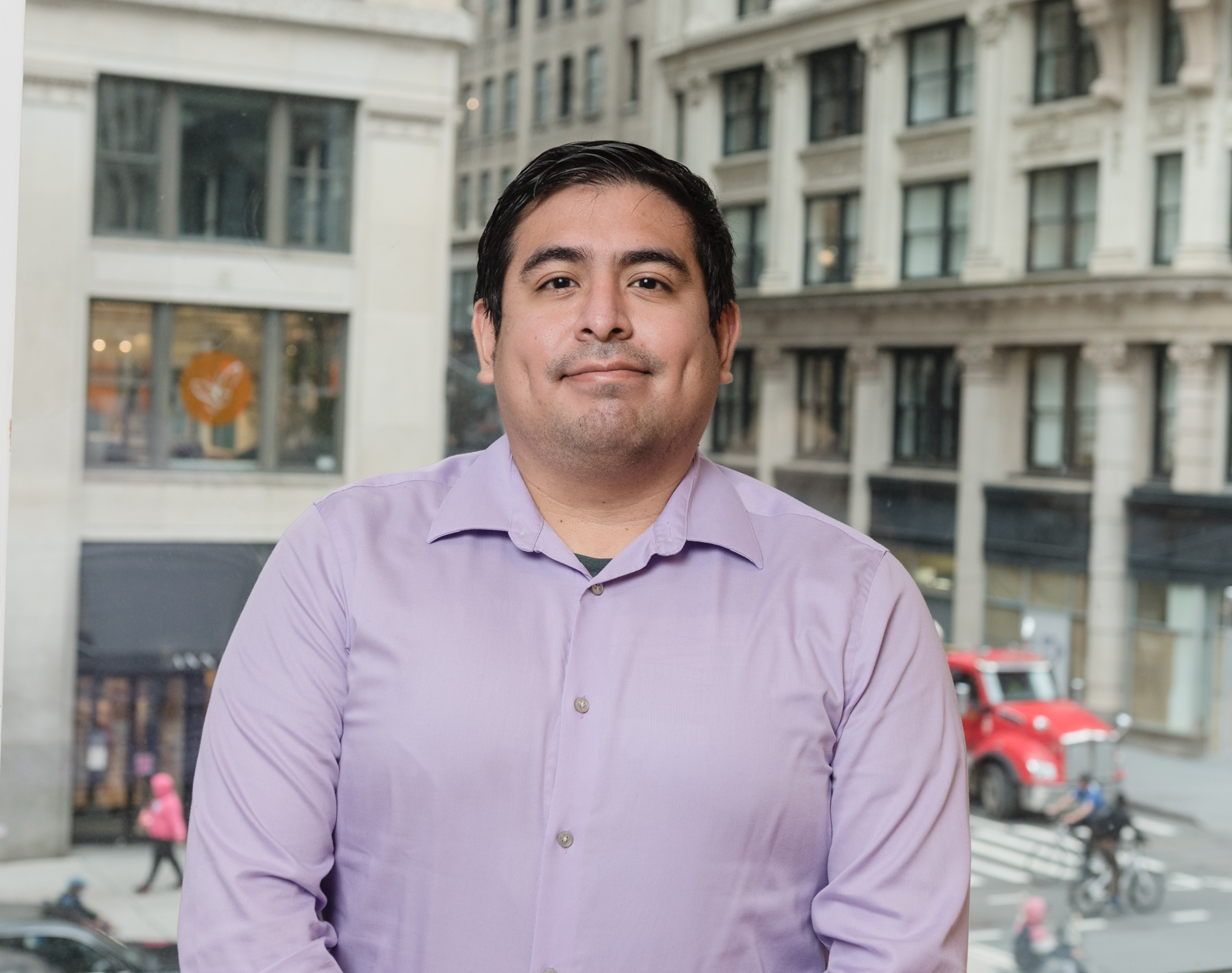 Headshot of a man in his 30s who has heritage from Peru with light skin tone and black short hair. He is wearing a purple button up and smiling at the camera.