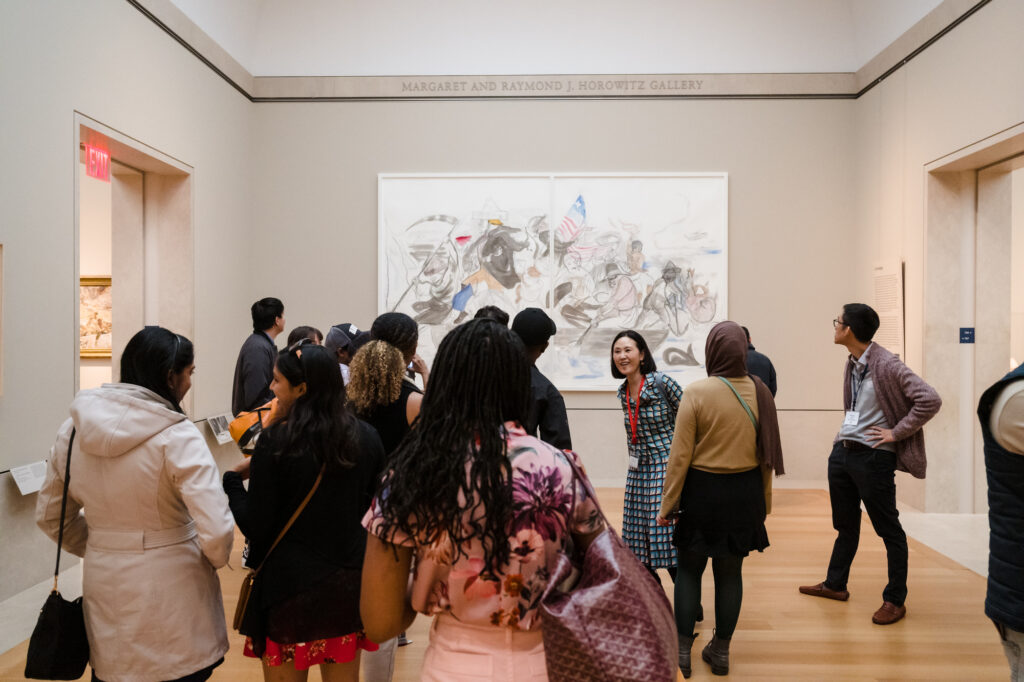 Photograph of a group of people standing in a museum gallery viewing a modern painting. 