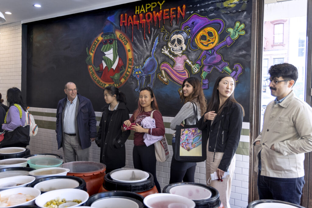 Photograph of a group of people standing around in front of a mural that says "Happy Halloween" and a few illustrated characters.