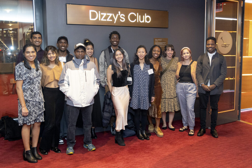 Photograph of a group of people posing in front of a sign that reads "Dizzy's Club". They are all dressed up.