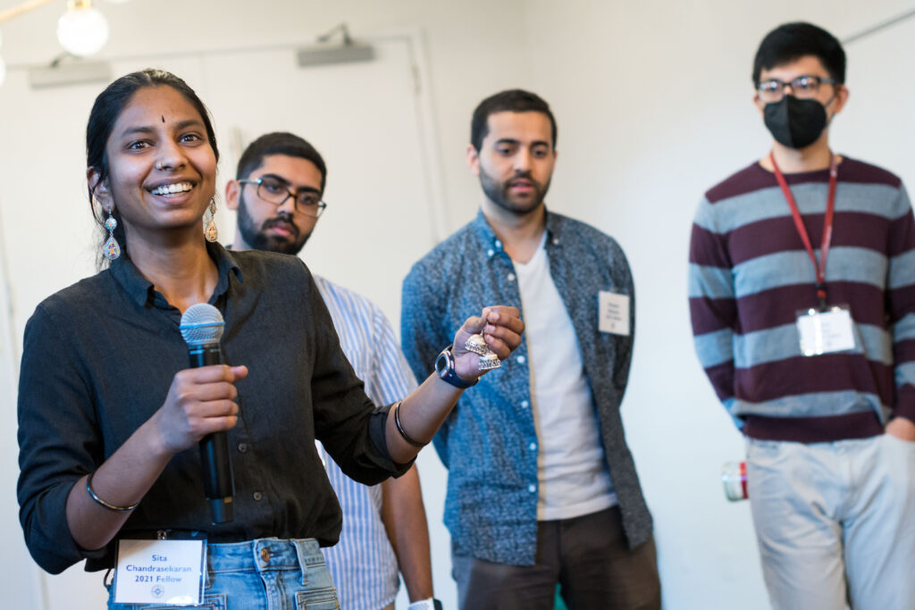 Photograph of four people looking just off camera. The person on the left is the only woman and she is speaking.