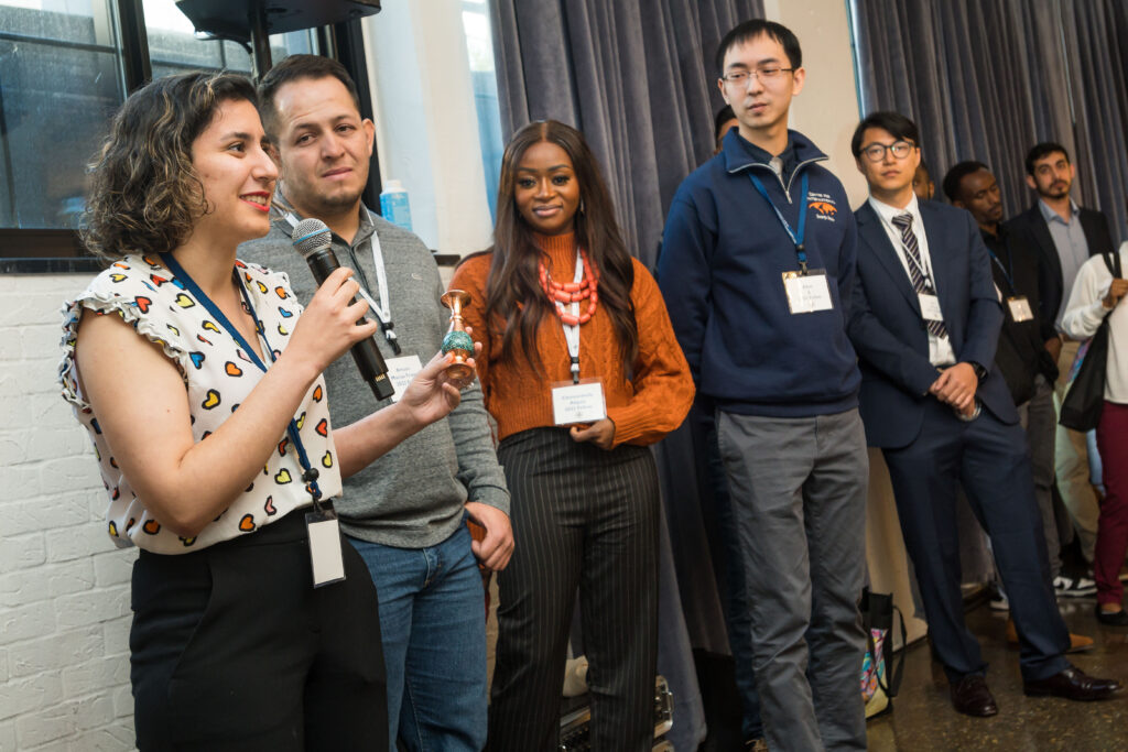 Photograph of a group of people standing, all with lanyards on. The woman on the left has a microphone in hand while the others look on. 