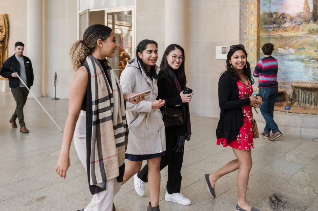 Photograph of four women in their 20s, walking and in conversation. 