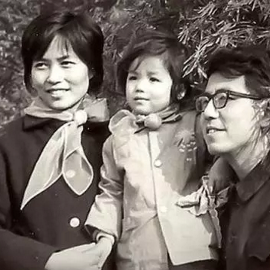 Black and white photograph of a family, mom, dad and young girl. They are looking off camera and are dressed up. 