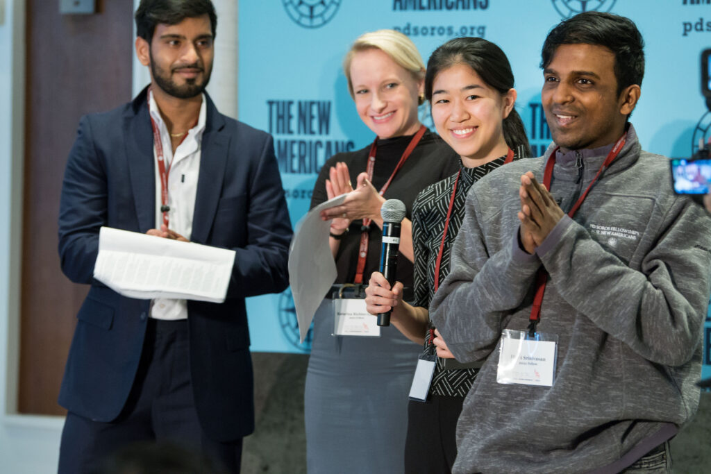 Hari stands with his hands clasped in thanks with three Fellows standing behind him at the 2023 Fall Conference.