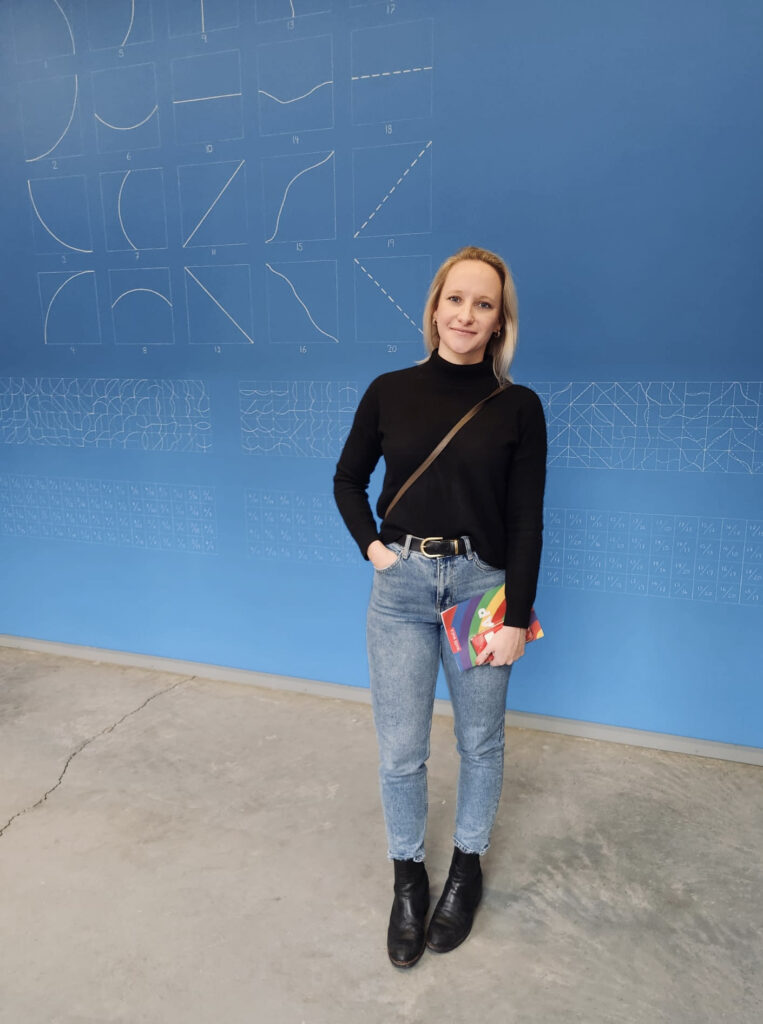 Photograph of a woman in her 20s standing in front of a wall of Sol le Witt art.