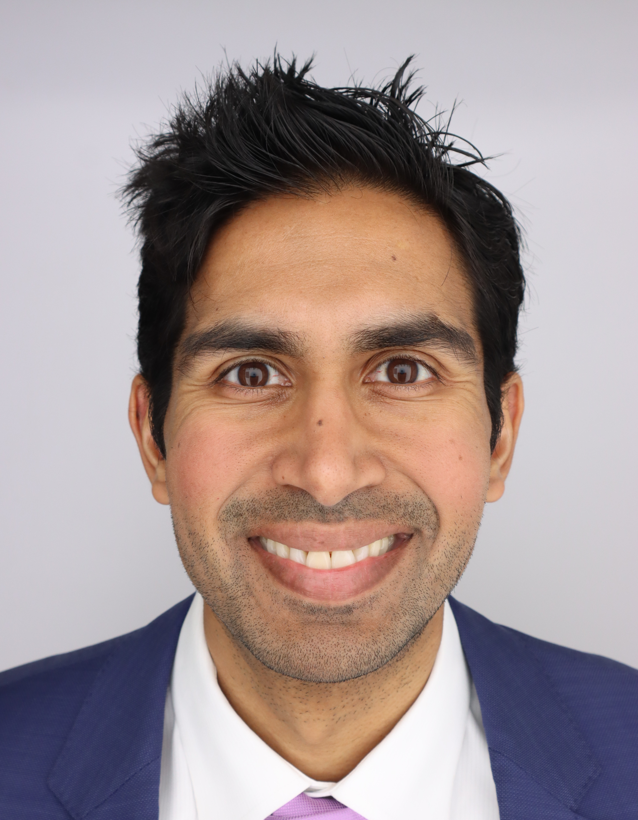 Aadel Chaudhuri headshot - he is smiling and looking directly at the camera and you can see the top of his jacket, collar and tie.