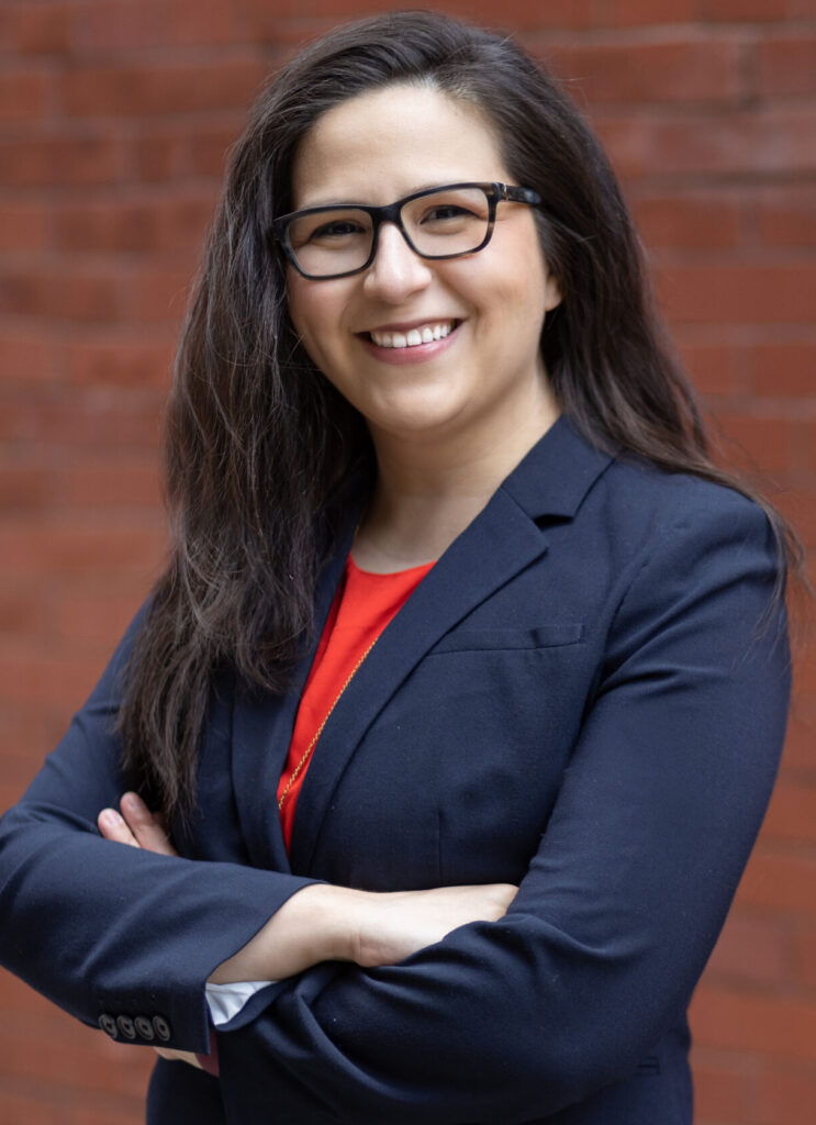 A photo of Carolina M. Montaño who is wearing a blazer and has her arms crossed and is wearing glasses.