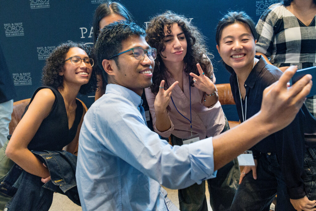 A group of 2024 Fellows stand around a camera for a selfie. 