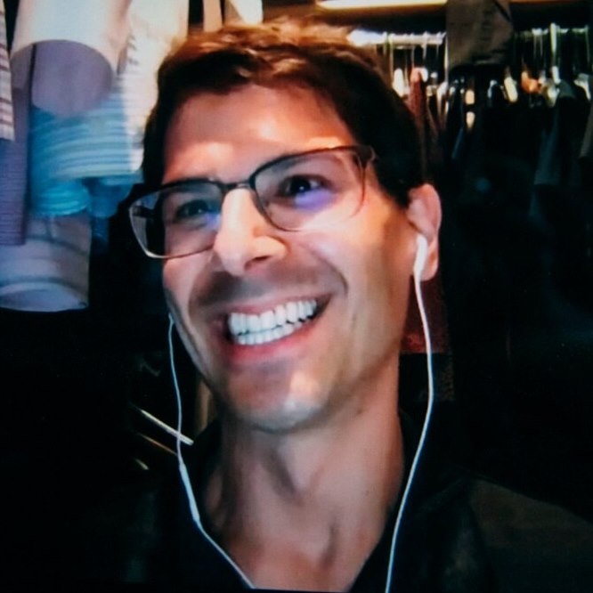 A casual photo smiling Dov Fox with ear plugs in and looking away from the camera.